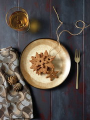 Vogelperspektive auf einen Teller aus der Serie Shade Matt Earth mit Plätzchen in Schneeflockenform, einem Glas mit Getränk, einer Gabel und einem gemusterten Tuch.