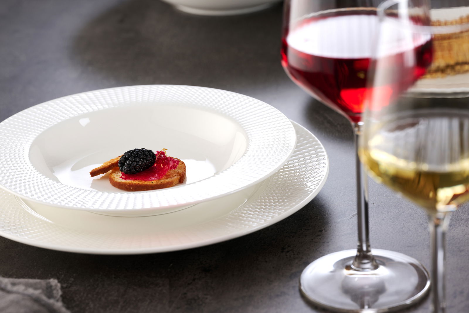 Suppenteller 27cm mit feiner Struktur, von oben fotografiert, serviert mit einer kleinen Vorspeise und umgeben von Weingläsern.