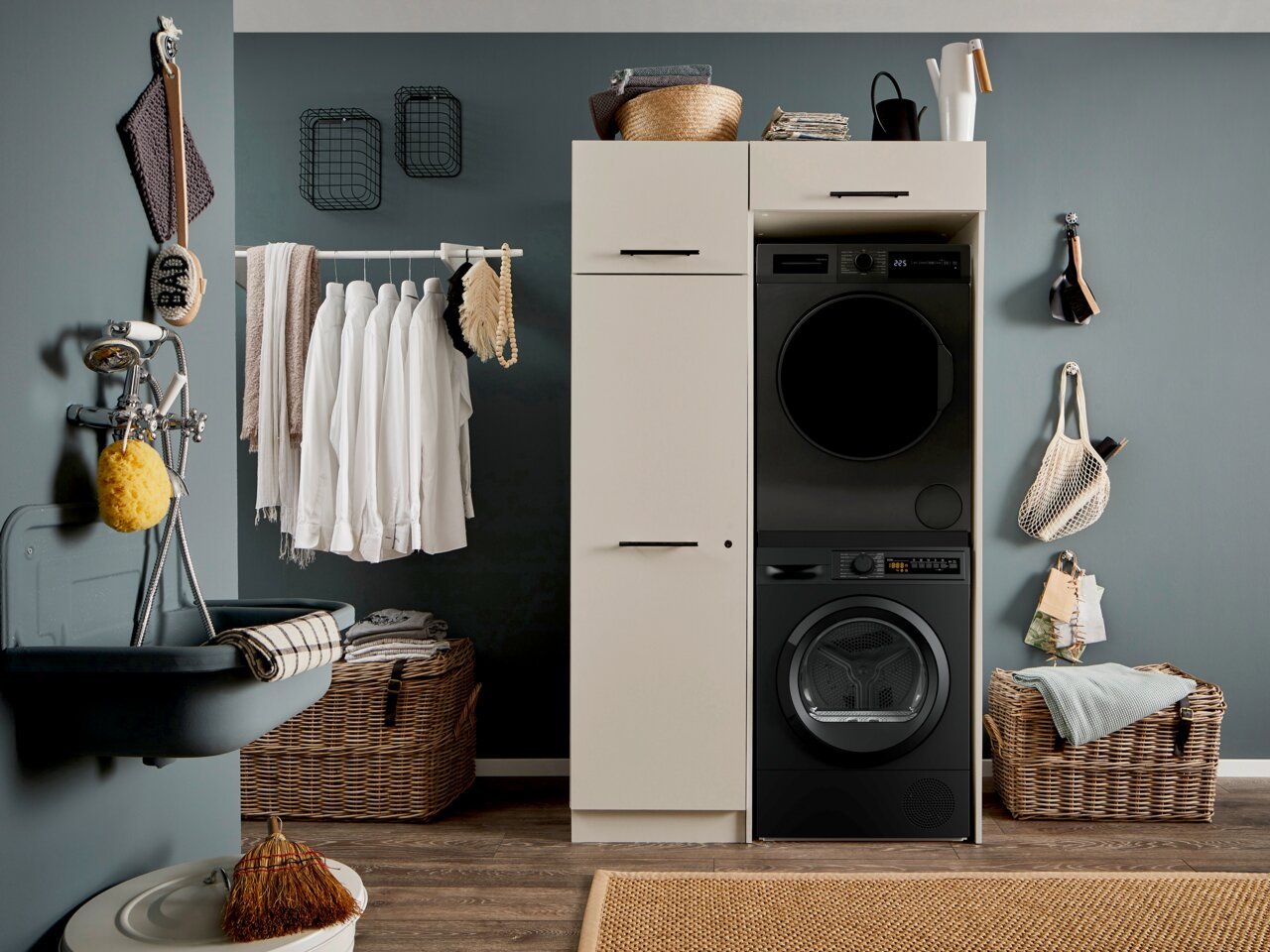 XORA Hauswirtschaftsraum-Kombi PRIMUS Moderner Hauswirtschaftsraum mit weißem Waschmaschinen-Schrank und schwarzem Waschturm (Waschmaschine und Trockner) neben Waschbecken, Wäsche und Körben, Frontalansicht.
