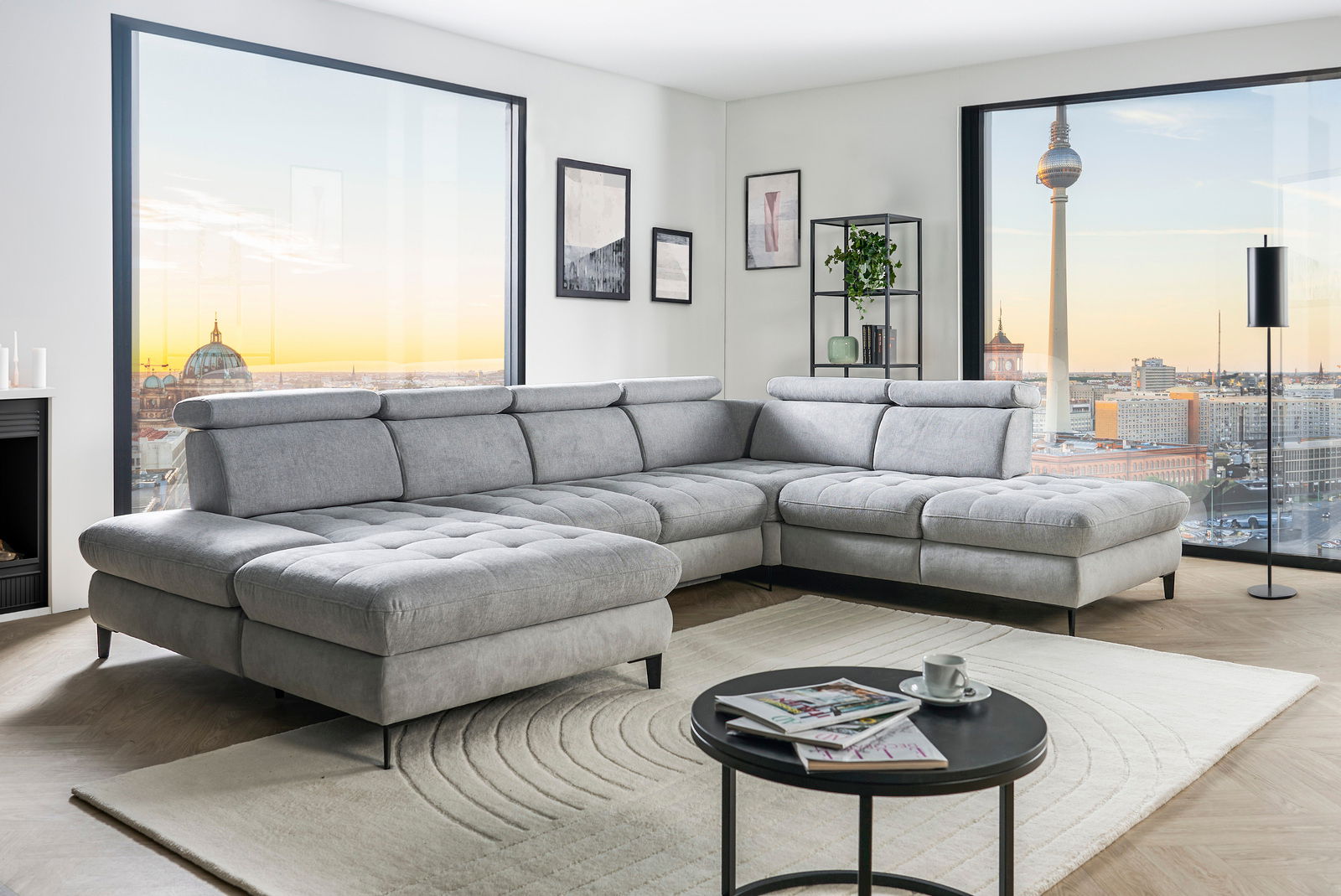 Graue Rundecke (L) in modernem Wohnzimmer mit Blick auf die Stadt, von vorne links gesehen.