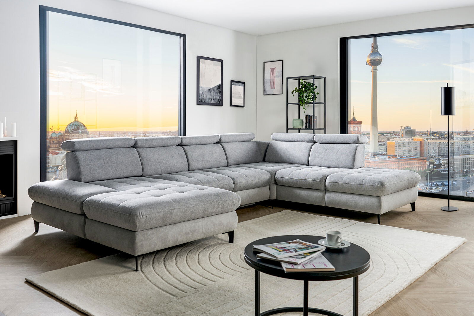 Graue Rundecke (L) in modernem Wohnzimmer mit Blick auf die Stadt, von vorne links gesehen.