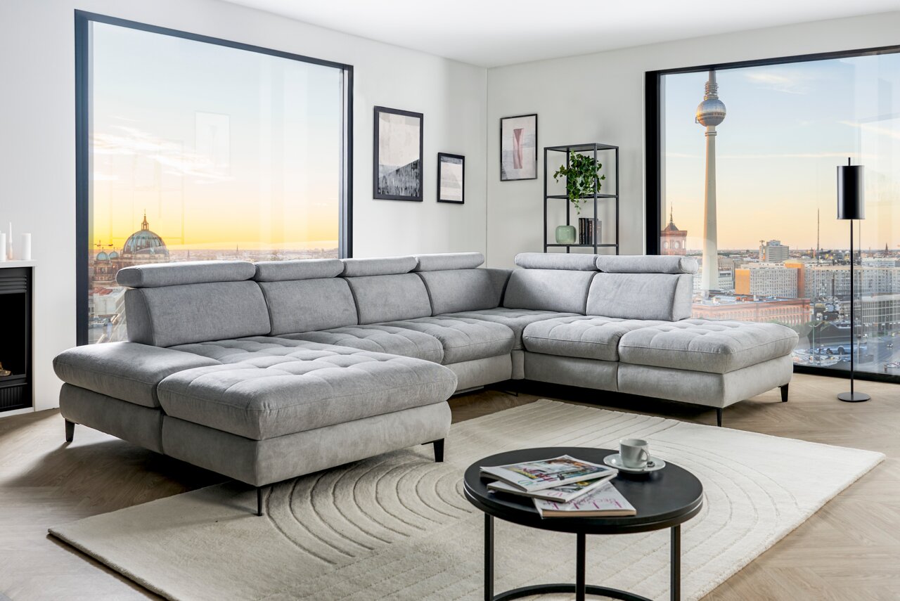 Graue Rundecke (L) in modernem Wohnzimmer mit Blick auf die Stadt, von vorne links gesehen.
