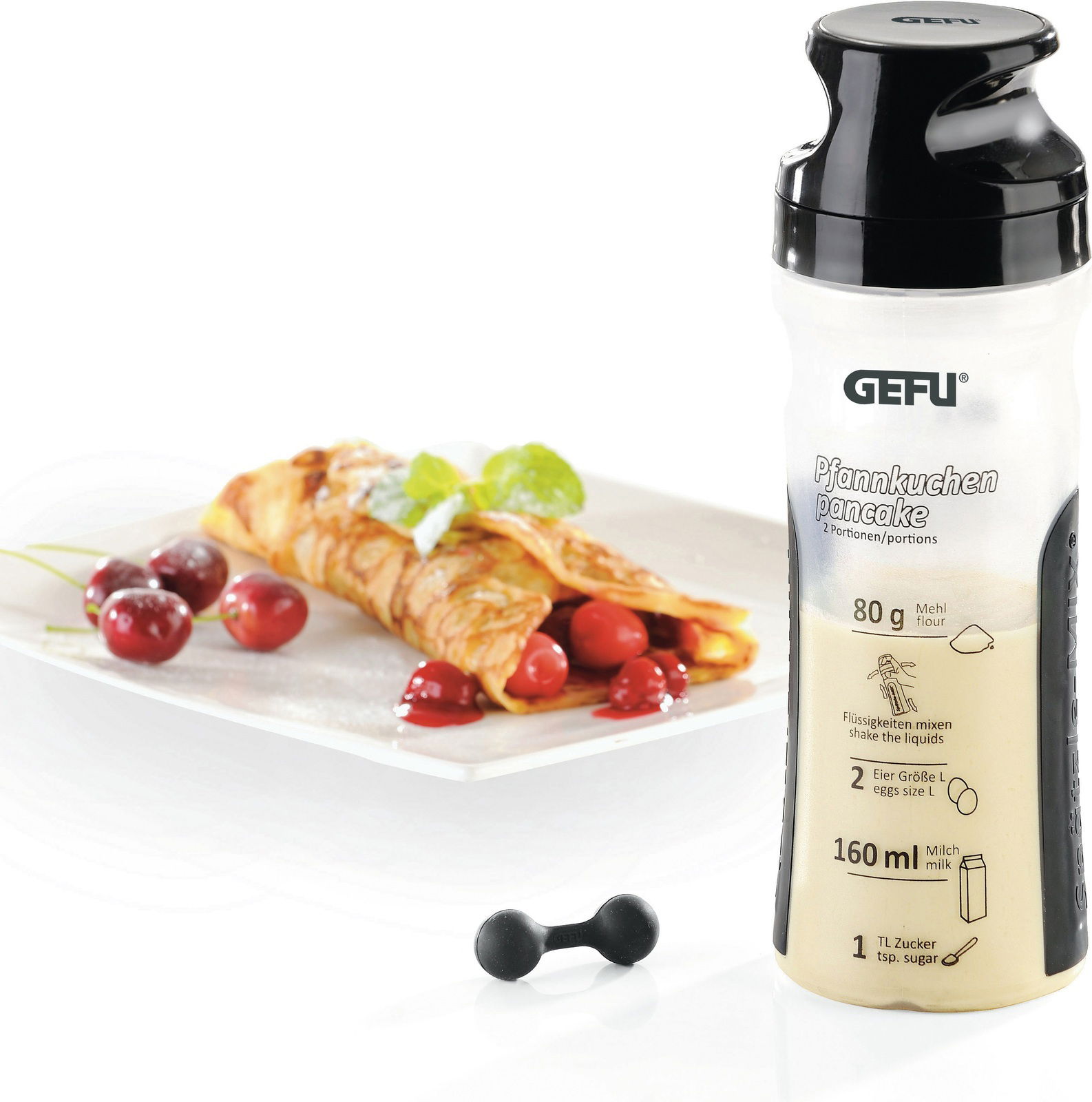 Crepes-Pfannkuchen Mix in einer Flasche mit schwarzem Deckel, daneben ein Teller mit gefüllten Crepes und Kirschen, aus der Perspektive von vorne.