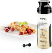 Crepes-Pfannkuchen Mix in einer Flasche mit schwarzem Deckel, daneben ein Teller mit gefüllten Crepes und Kirschen, aus der Perspektive von vorne.