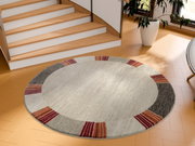 Runder Frisé-Teppich mit einem modernen Design in Beige, Grau und Rottönen, auf einem Holzfußboden vor einer Treppe platziert. Perspektive von oben.
