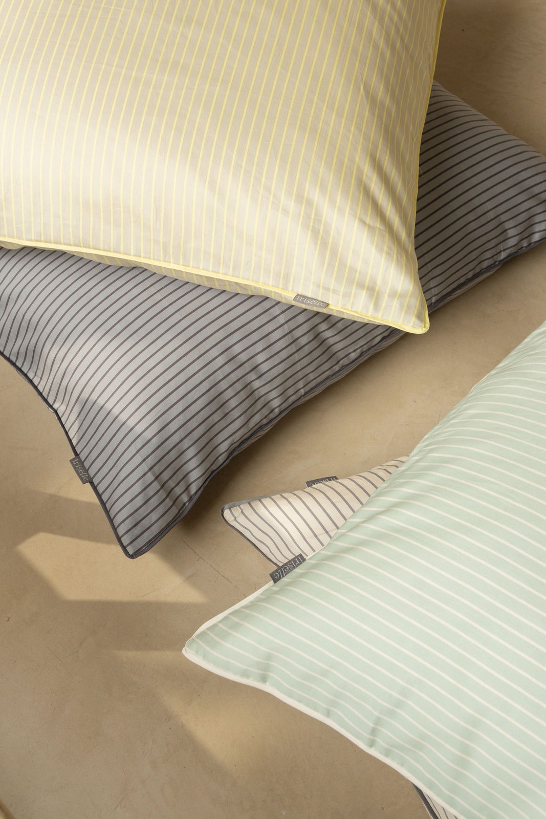 Blick von oben auf gestreifte Bettwäsche in verschiedenen Farben: Gelb, Grau, Weiß und Mintgrün.