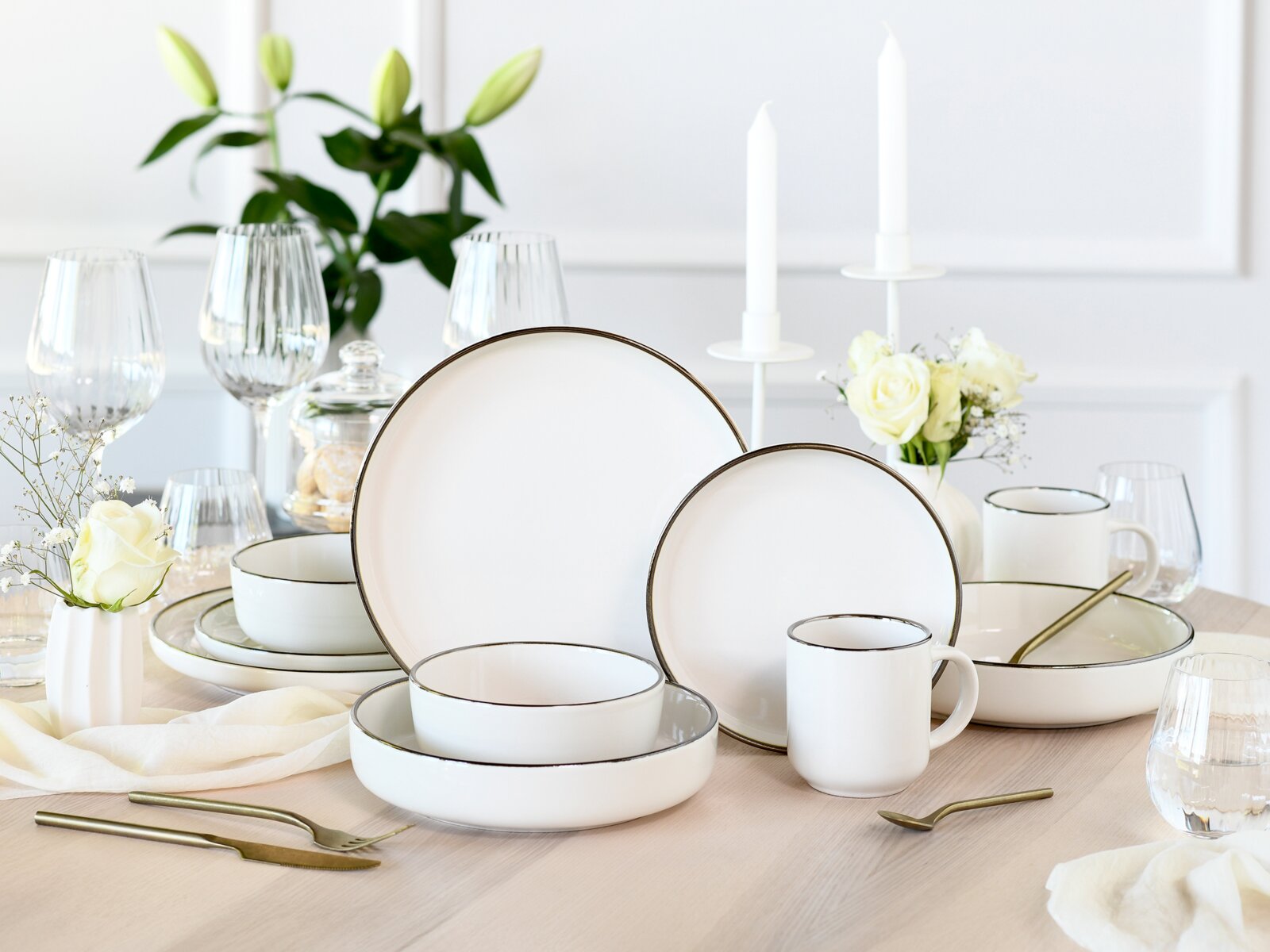 Creatable Kombiservice 10-tlg NORDIC FESTIVE Elegantes weißes Geschirrset mit feinem dunklem Rand (Teller, Schalen und Becher) auf gedecktem Esstisch mit Gläsern und weißen Blumen, fotografiert in leicht erhöhter Frontperspektive.