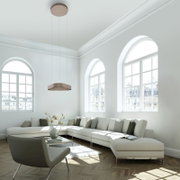 Moderne, flache Pendelleuchte in Bronze/Beige an drei dünnen Kabeln über einem hellen Wohnzimmer mit großem Ecksofa und Bogenfenstern, Ansicht leicht von unten nach oben
