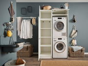 Hauswirtschaftsraum mit Waschmaschine und Trockner in einem Hochschrank, offene Regale, Wäschekorb und Waschbecken, seitliche Perspektive