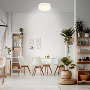 Moderne runde LED-Deckenleuchte in Weiß, eingeschaltet, in einem hellen Esszimmer über dem Esstisch – Ansicht leicht von unten/Frontalperspektive