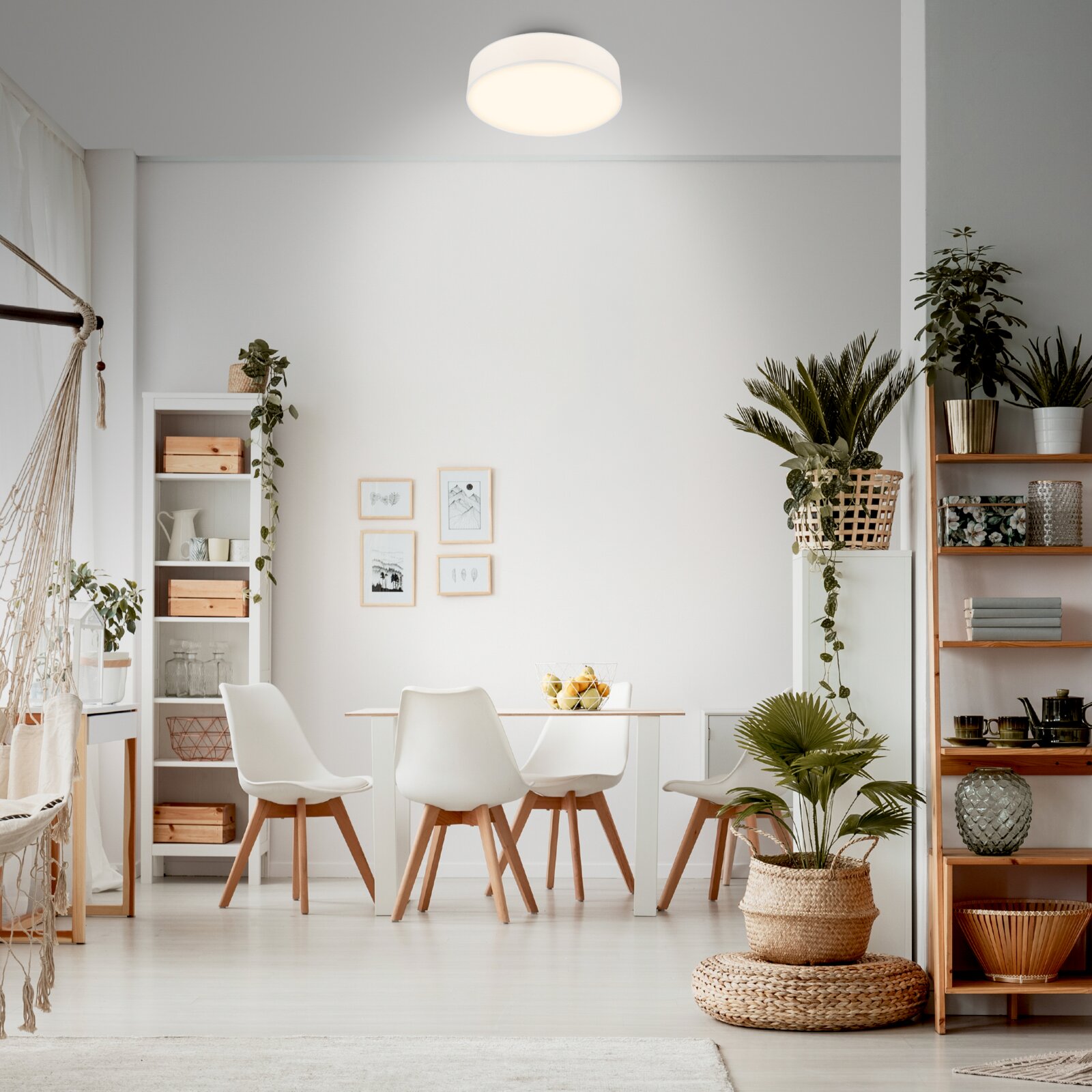 Moderne runde LED-Deckenleuchte in Weiß, eingeschaltet, in einem hellen Esszimmer über dem Esstisch – Ansicht leicht von unten/Frontalperspektive