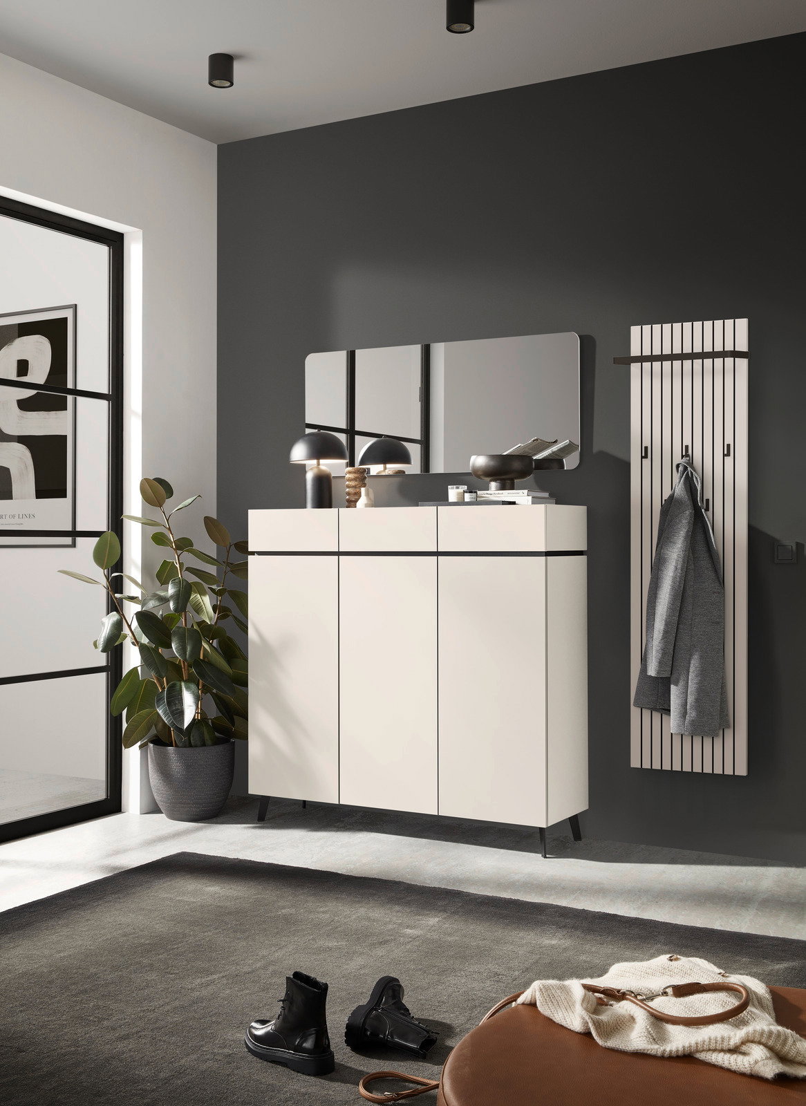 Voleo Garderobenpaneel UNIQUE Modernes Garderobenpaneel in einem stilvollen Raum, frontal betrachtet. Es ist an einer dunklen Wand montiert und mit einem Mantel behängt. Daneben steht ein elegantes Sideboard mit Dekorationen und ein großer Spiegel.