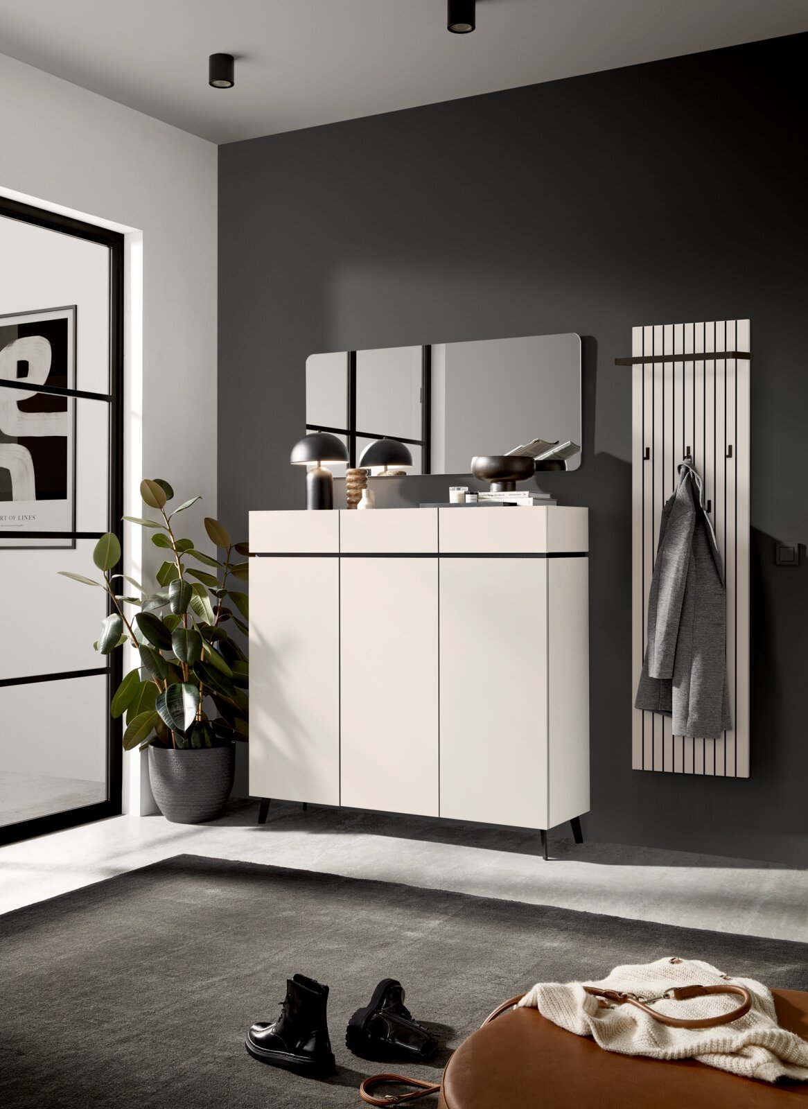 Modernes Garderobenpaneel in einem stilvollen Raum, frontal betrachtet. Es ist an einer dunklen Wand montiert und mit einem Mantel behängt. Daneben steht ein elegantes Sideboard mit Dekorationen und ein großer Spiegel.
