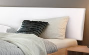 Close-up van een bedframe met een wit hoofdeinde, een grijs kussen en een bedovertrek met patroon, gezien vanaf de zijkant
