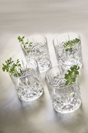 Vier kristallklare Whiskygläser mit dekorativem Schliff, von oben fotografiert, mit kleinen grünen Pflanzen als Dekoration.