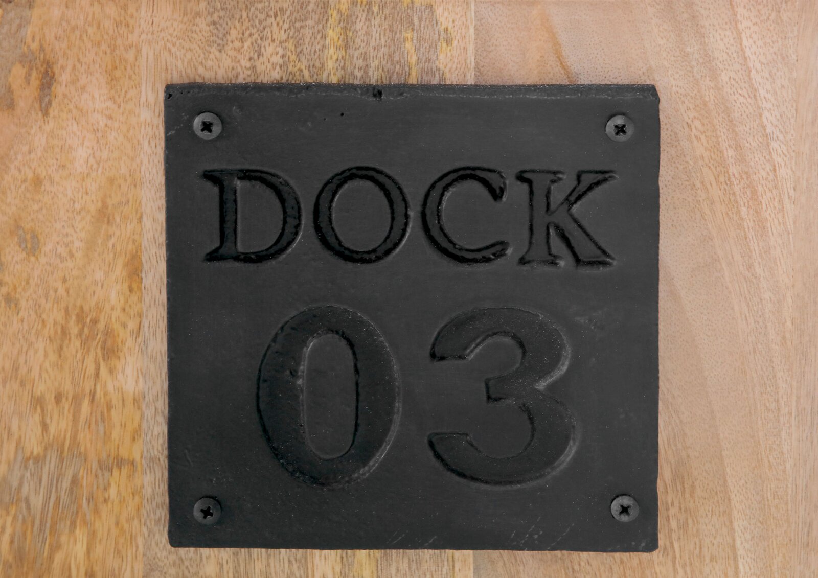 Nahaufnahme einer schwarzen Metallplatte mit der Aufschrift 'DOCK 03' auf einer Holzoberfläche.