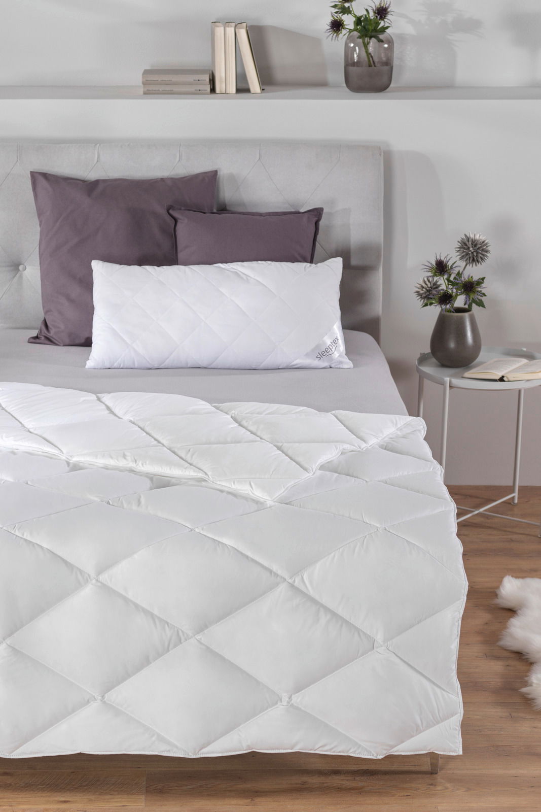 Gemütliches Schlafzimmer mit einem elegant drapierten Ganzjahresbett 155x220 cm in Weiß, aufgenommen aus einer leicht erhöhten Perspektive.