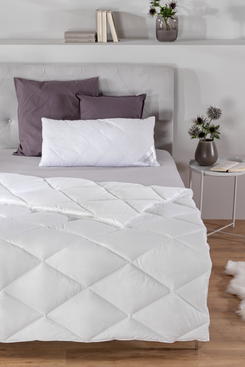 Gemütliches Schlafzimmer mit einem elegant drapierten Ganzjahresbett 155x220 cm in Weiß, aufgenommen aus einer leicht erhöhten Perspektive.