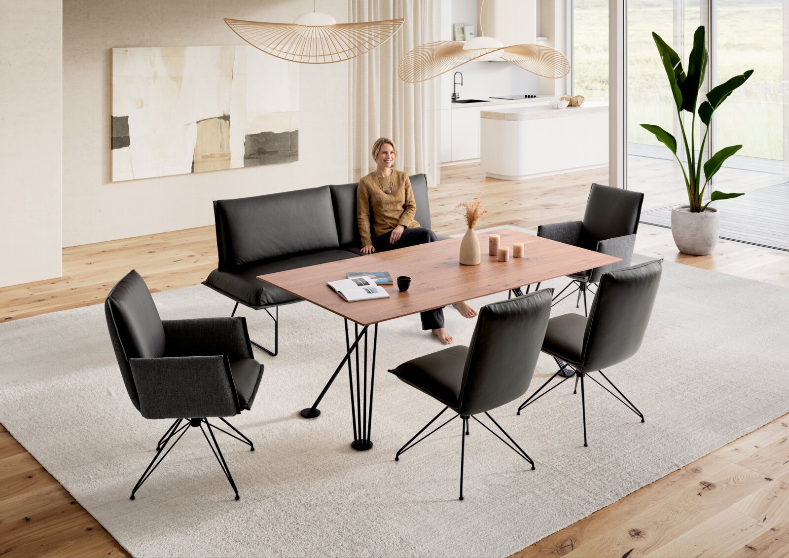 Modernes Esszimmer mit rechteckigem Holzesstisch auf schwarzem Metallgestell, schwarzer Sitzbank und vier schwarzen Polsterstühlen auf hellem Teppich, Perspektive: leicht erhöhte Frontansicht schräg von vorne.