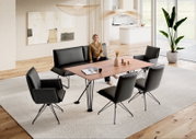 Modernes Esszimmer mit rechteckigem Holzesstisch auf schwarzem Metallgestell, schwarzer Sitzbank und vier schwarzen Polsterstühlen auf hellem Teppich, Perspektive: leicht erhöhte Frontansicht schräg von vorne.