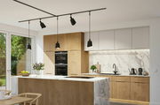 Moderne Küche mit Holz- und Marmorelementen, zentraler Kücheninsel und hängenden schwarzen Lampen, Blick von der Seite.