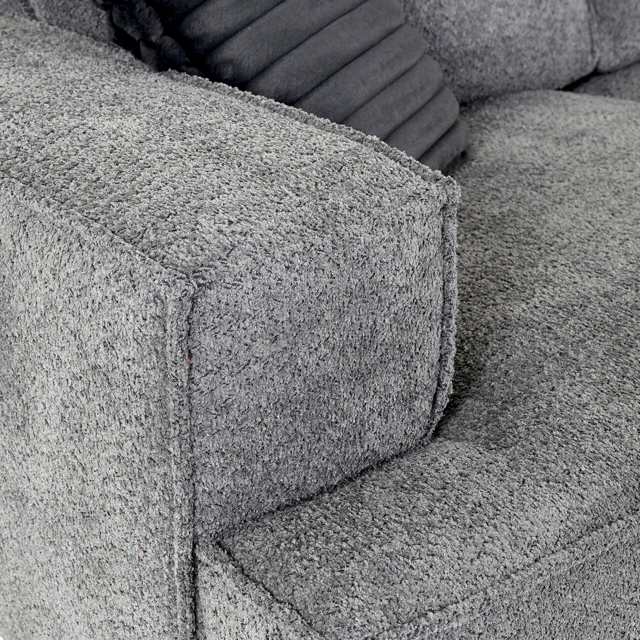 Nahaufnahme einer grauen Sofaecke mit strukturiertem Stoffbezug und einem dekorativen Kissen, Perspektive von oben.