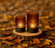 Zwei Akku-Windlichter auf einem Holzbrett, umgeben von Herbstblättern, aus seitlicher Perspektive fotografiert.