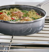 Graue Servierpfanne mit Hähnchenschenkeln und Reis, seitliche Perspektive