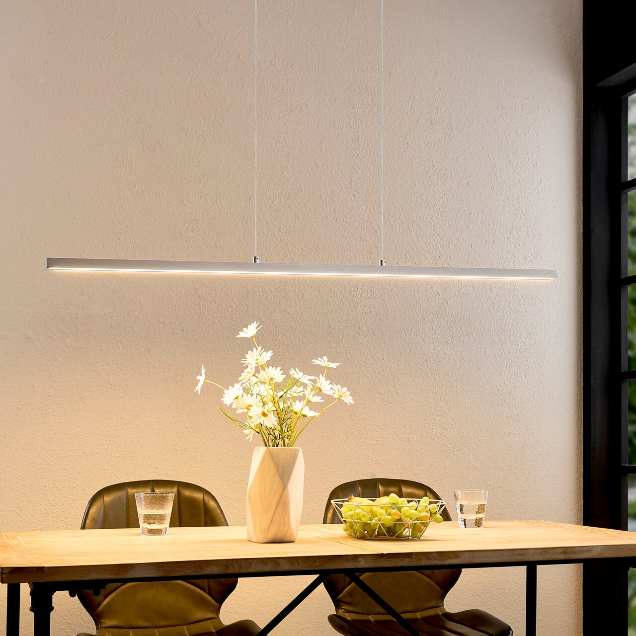 Minimalistische, strakke LED-hanglamp in wit boven een houten tafel met een vaas en een fruitschaal, vooraanzicht op ooghoogte.