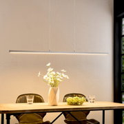Minimalistische, strakke LED-hanglamp in wit boven een houten tafel met een vaas en een fruitschaal, vooraanzicht op ooghoogte.