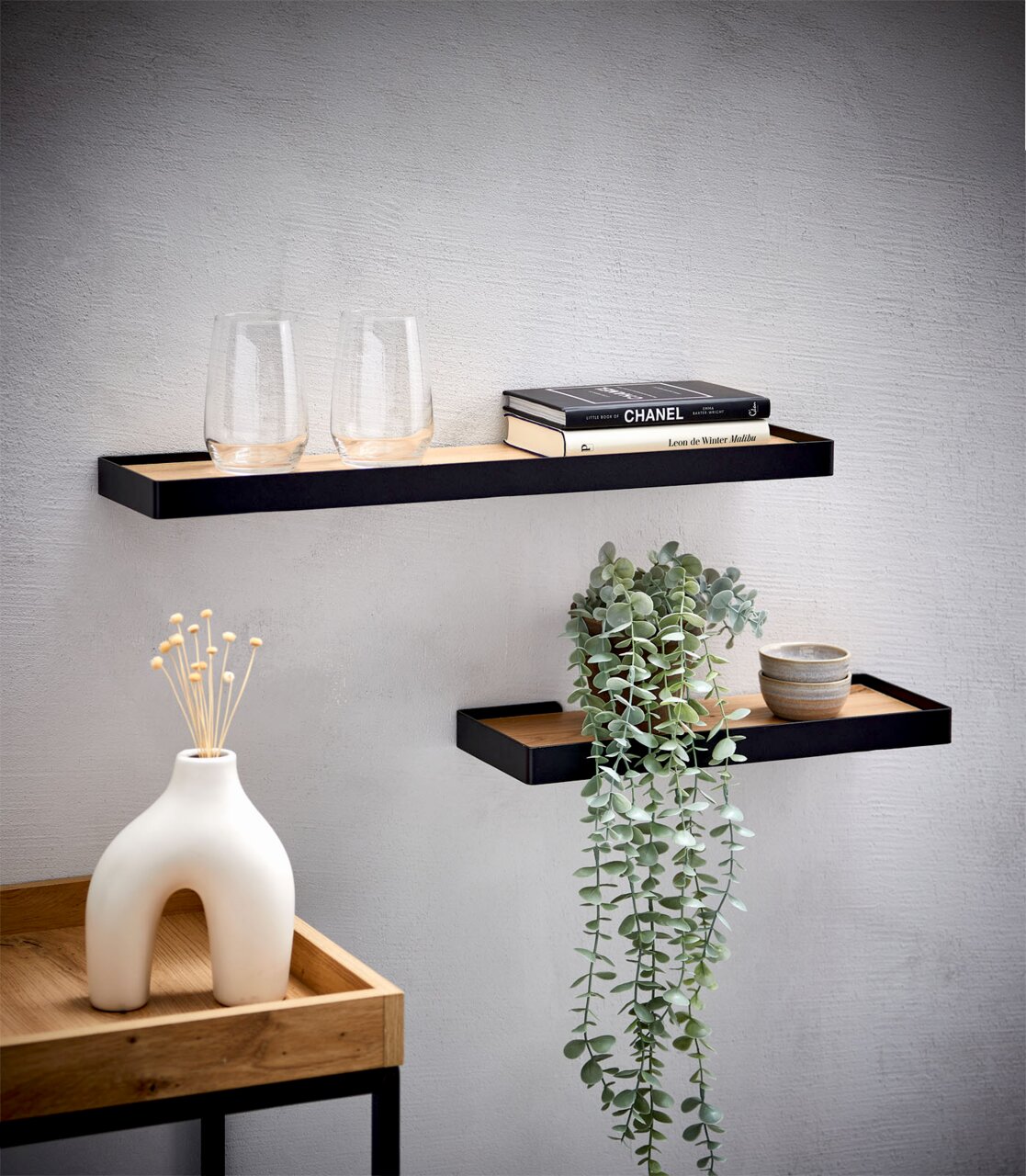 XORA Wandboard 60cm RICKY Zwei schwebende Wandregale mit schwarzem Metallrahmen und Holzablage, dekoriert mit Gläsern, Büchern, Schalen und einer Hängepflanze, aus frontaler Perspektive leicht von oben