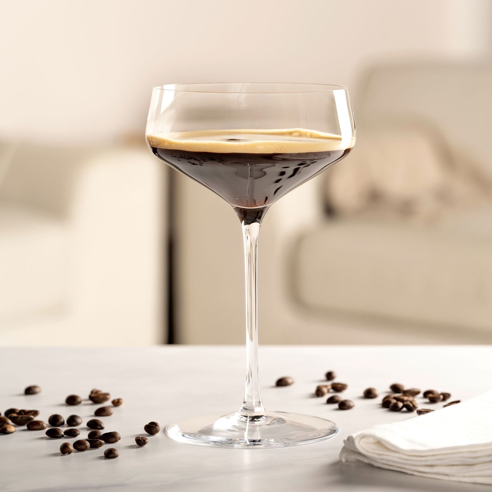 Elegante Champagnerschale mit dunklem Getränk, umgeben von Kaffeebohnen, auf einem Tisch in einem modernen Wohnzimmer.