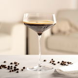 Elegante Champagnerschale mit dunklem Getränk, umgeben von Kaffeebohnen, auf einem Tisch in einem modernen Wohnzimmer.