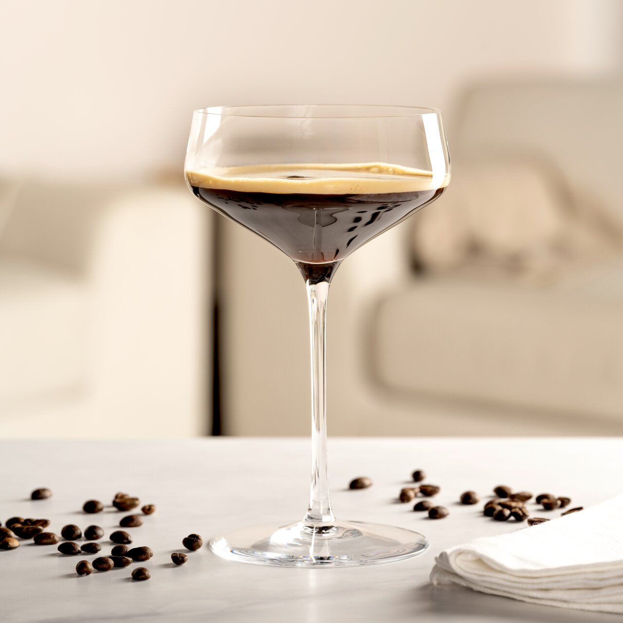 Elegante Champagnerschale mit dunklem Getränk, umgeben von Kaffeebohnen, auf einem Tisch in einem modernen Wohnzimmer.