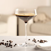 Elegante Champagnerschale mit dunklem Getränk, umgeben von Kaffeebohnen, auf einem Tisch in einem modernen Wohnzimmer.