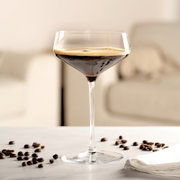 Elegante Champagnerschale mit dunklem Getränk, umgeben von Kaffeebohnen, auf einem Tisch in einem modernen Wohnzimmer.