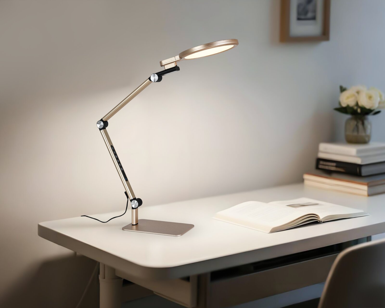 Moderne LED-Schreibtischlampe in Champagnergold mit verstellbarem Gelenkarm und flachem Leuchtenkopf auf weißem Schreibtisch neben offenem Buch, perspektivisch in seitlicher 3/4-Ansicht von links