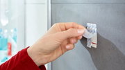 Hand zieht tesa Powerstrips Waterproof von einer glatten Wandoberfläche ab, seitliche Perspektive
