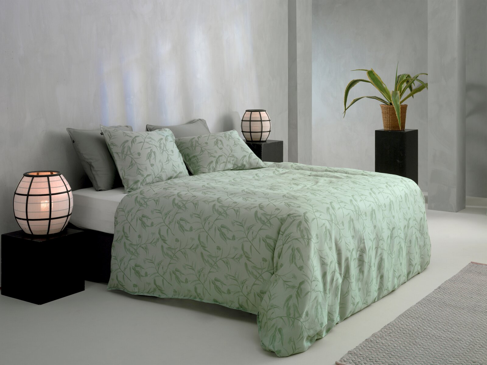 ZO!HOME Bettwäsche FIORI DI SATINADO Bett mit grüner Bettwäsche und Pflanzenmuster, seitliche Perspektive, dekoriert mit Kissen und Lampen.