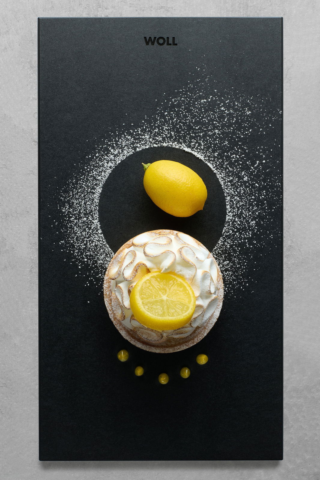 Frontalansicht eines Frühstückssets mit einer Zitrone und einem Kuchen auf einem schwarzen Untergrund, dekoriert mit Puderzucker.