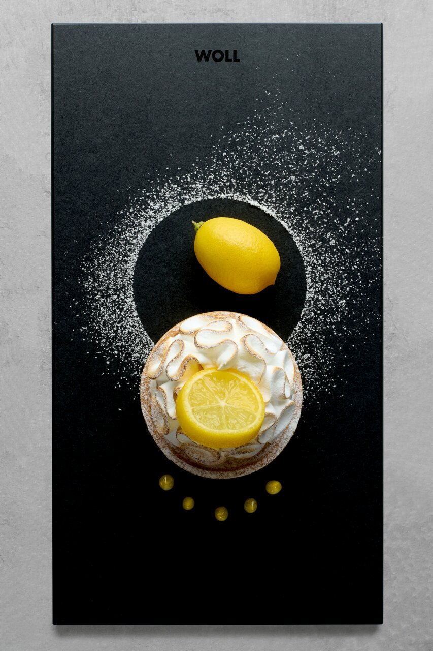 Frontalansicht eines Frühstückssets mit einer Zitrone und einem Kuchen auf einem schwarzen Untergrund, dekoriert mit Puderzucker.