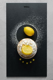 Frontalansicht eines Frühstückssets mit einer Zitrone und einem Kuchen auf einem schwarzen Untergrund, dekoriert mit Puderzucker.