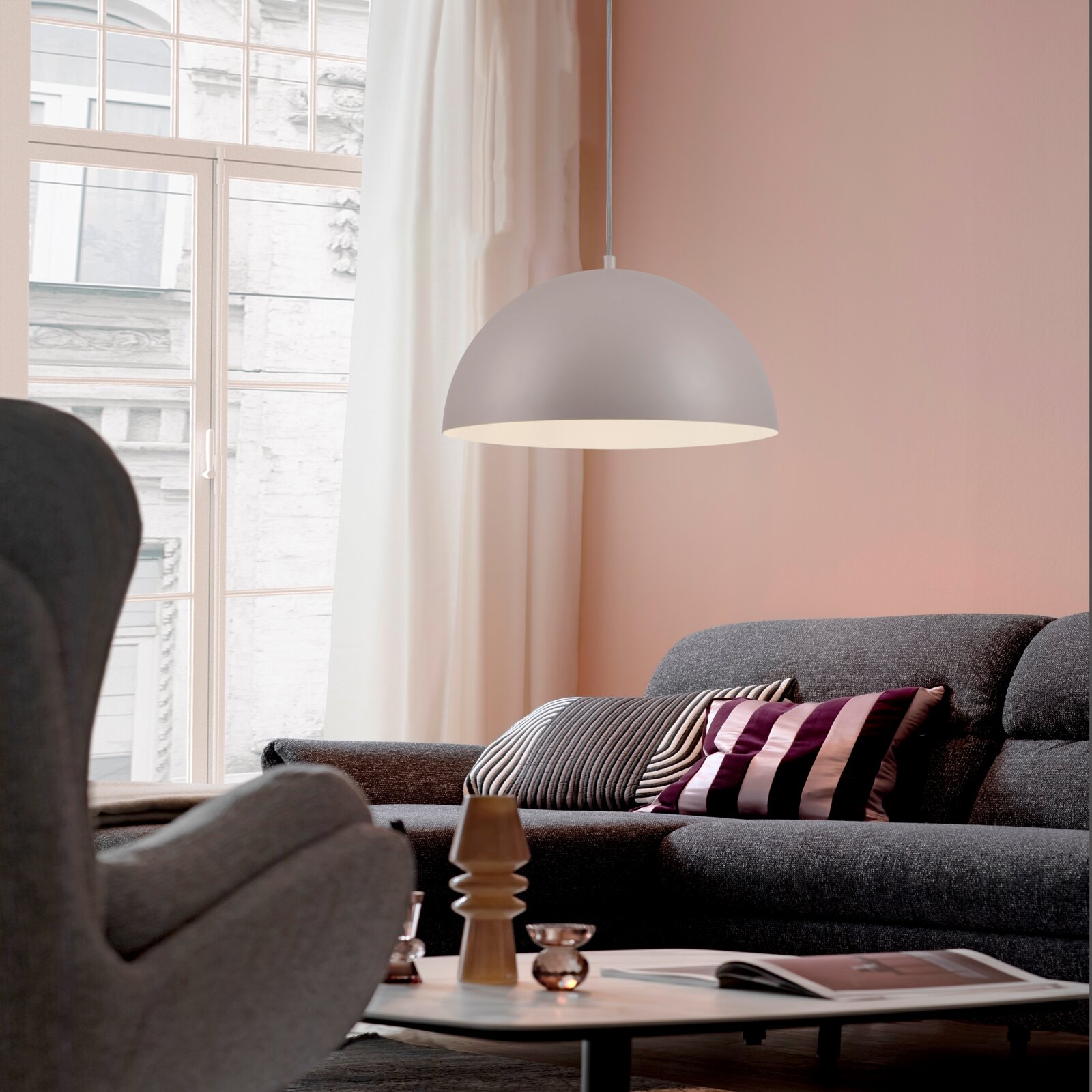 Weiße, halbkugelförmige Pendelleuchte im modernen Wohnzimmer über grauem Sofa, frontal in leichter Seitenansicht aufgenommen