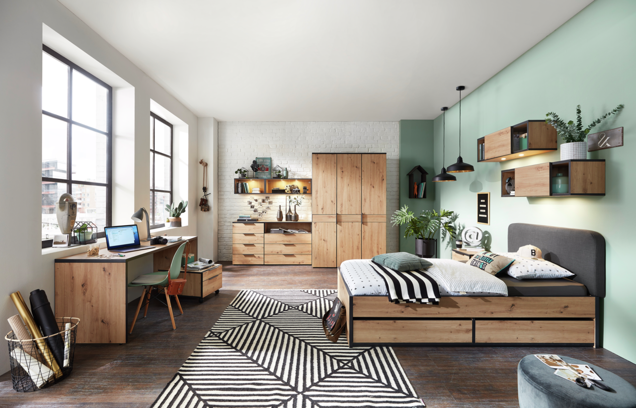 Modernes Jugendzimmer mit Schreibtisch, Rollcontainer, Bett und Stauraummöbeln in Holzoptik, aus der Perspektive von links nach rechts fotografiert.