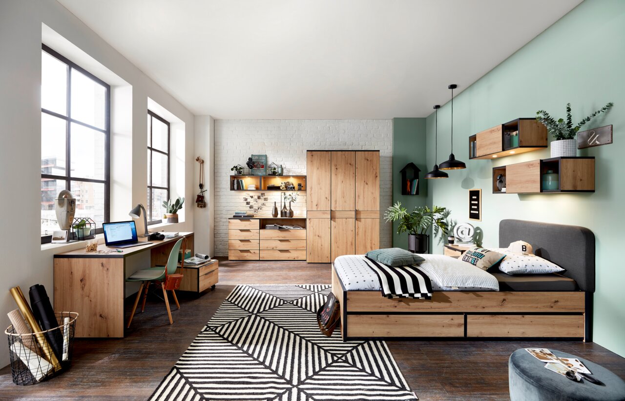 Modernes Jugendzimmer mit Schreibtisch, Rollcontainer, Bett und Stauraummöbeln in Holzoptik, aus der Perspektive von links nach rechts fotografiert.