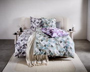 Bed met modern beddengoed met een geometrisch patroon in grijs, blauw en paars, gefotografeerd van voren.