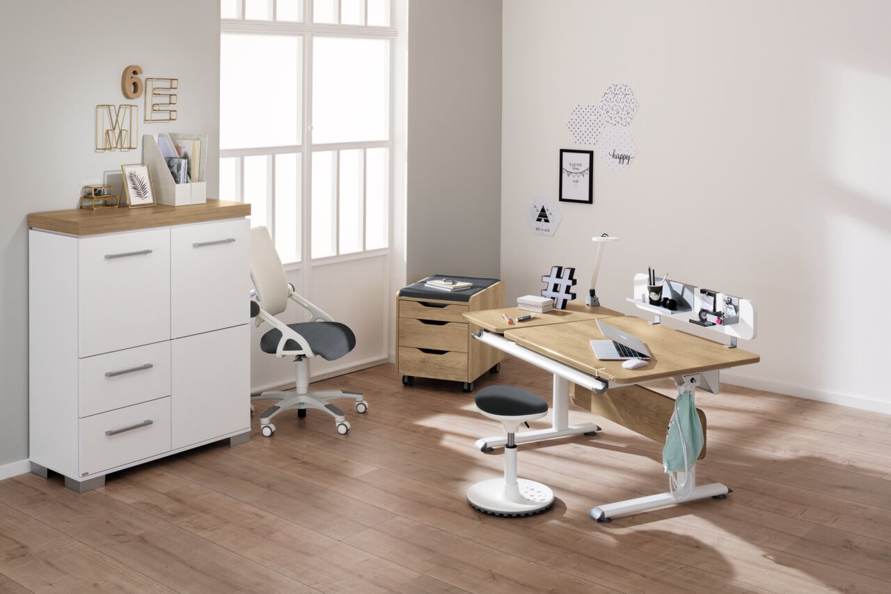 Moderner Schreibtisch in einem hellen Raum, mit ergonomischem Stuhl und Stauraum, aus seitlicher Perspektive fotografiert.