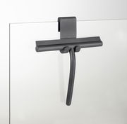 Moderner Badezimmerwischer aus Silikon in dunkler Farbe, an einer Glaswand hängend, seitliche Perspektive.