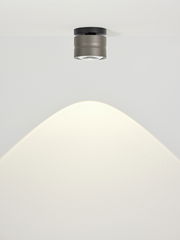 Moderne LED-Deckenleuchte in zylindrischer Form, von unten betrachtet, mit warmem Lichtstrahl auf weißer Decke.