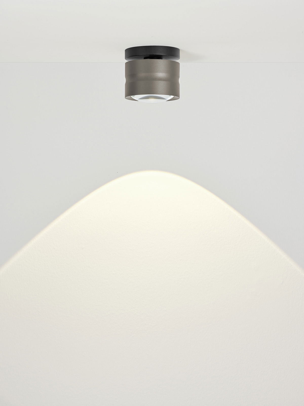 Moderne LED-Deckenleuchte in zylindrischer Form, von unten betrachtet, mit warmem Lichtstrahl auf weißer Decke.